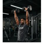 Person performing shoulder exercises with dumbbells in a gym, highlighting effective shoulder training techniques.