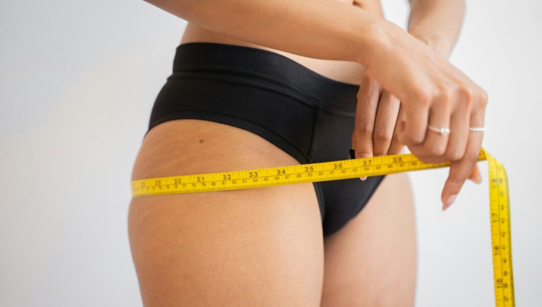 Frau misst Taille und Hüfte mit Maßband